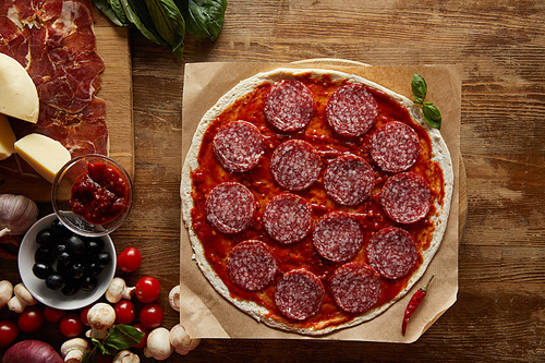 Top view of pizza with salami and tomato sauce on wooden background