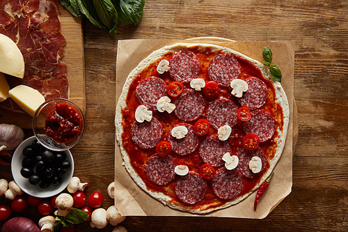 Top view of pizza with salami, mushrooms and tomato sauce on wooden background
