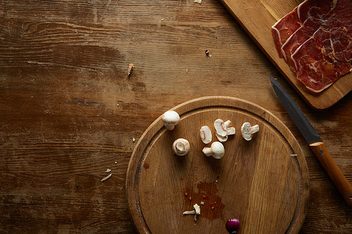 Top view of mushrooms, prosciutto and knife on wooden background