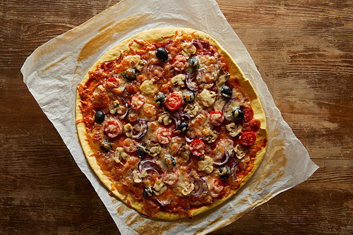 Top view of delicious pizza with cherry tomatoes, olives and parmesan on parchment paper on wooden background