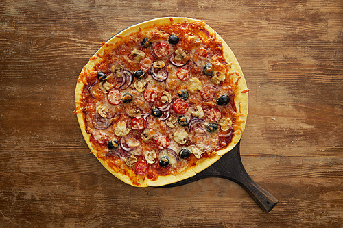 Top view of delicious pizza with cherry tomatoes, olives and parmesan on cutting board on wooden background
