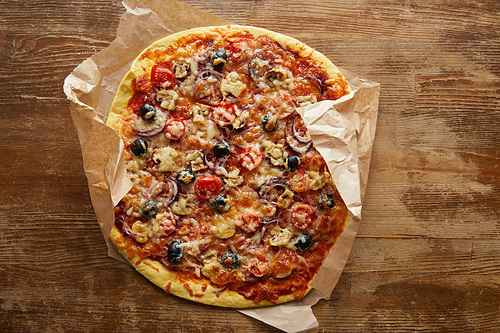Top view of delicious pizza on parchment paper on wooden background