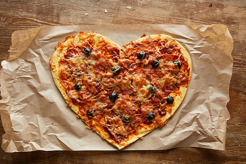 top view of delicious italian pizza in heart shape on baking paper on wooden table
