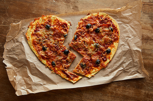 top view of delicious italian pizza in broken heart shape on baking paper on wooden table