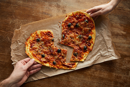cropped view of couple holding delicious italian pizza in broken heart shape on baking paper at wooden table
