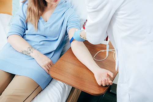 partial view of doctor using tourniquet for blood test in hospital