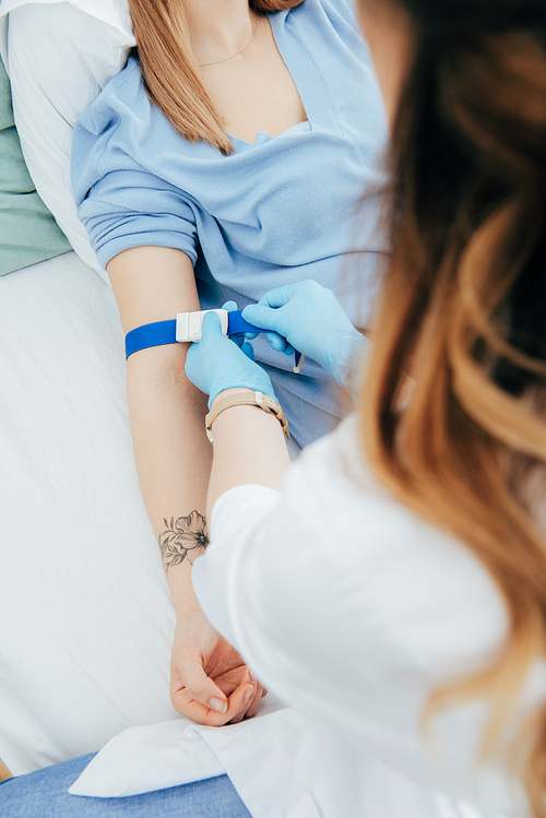 partial view of doctor using tourniquet for blood test in hospital