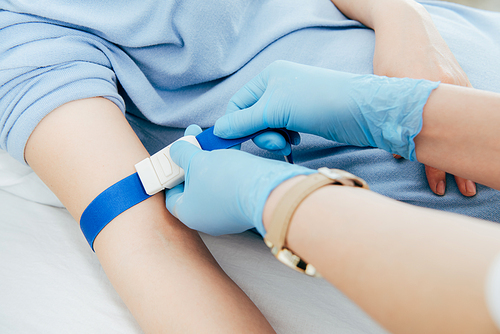 partial view of doctor using tourniquet for blood test in hospital