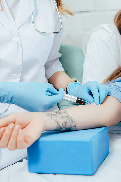 cropped view of donor and doctor with syringe obtaining blood sample