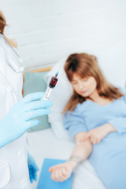 cropped view of doctor holding syringe with blood sample and donor lying on bed