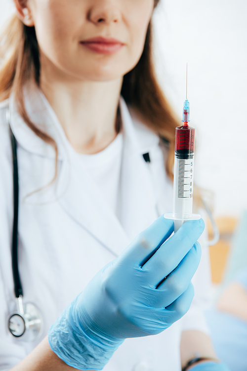 partial view of doctor in white coat holding syringe with blood sample