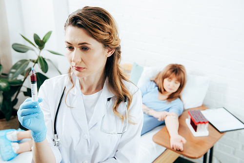 donor lying on bed and doctor holding syringe with blood sample