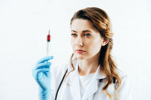 doctor in white coat holding syringe with blood sample on white