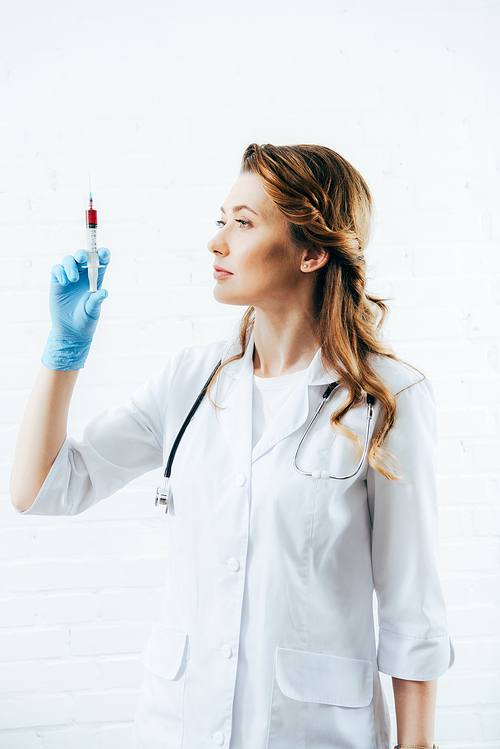 doctor in white coat holding syringe with blood sample on white