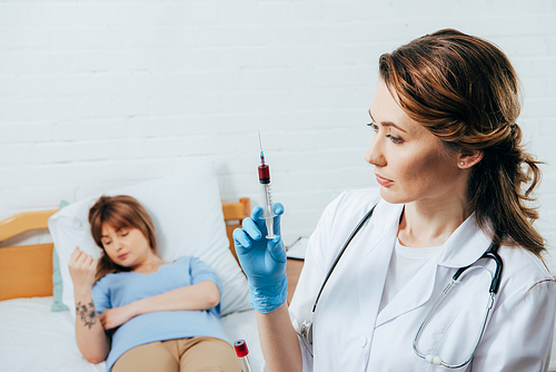 donor on bed and doctor holding syringe with blood sample