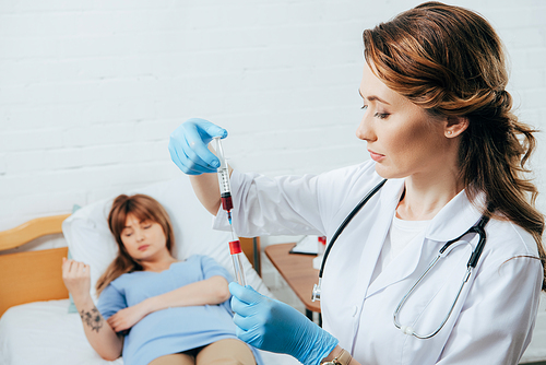 donor on bed and doctor holding syringe with blood sample and test tube