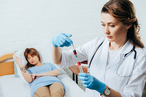 donor on bed and doctor holding syringe with blood sample and test tube