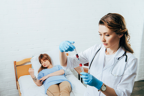 donor on bed and doctor holding syringe with blood sample and test tube