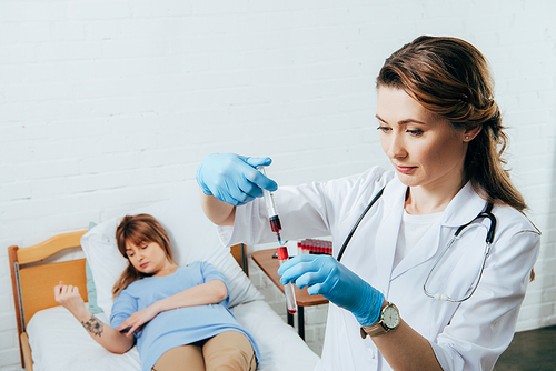 donor on bed and doctor holding syringe with blood sample and test tube