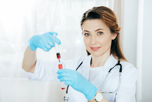 smiling doctor in latex gloves holding syringe with blood sample and test tube