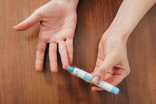 cropped view of woman holding blood lancet on wooden surface