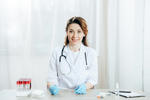 smiling doctor holding pipette and microscope slide with blood sample