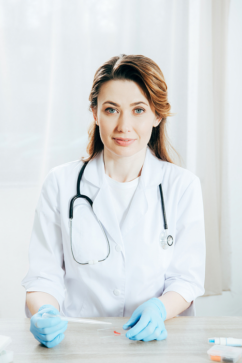 doctor in white coat and latex gloves holding pipette with blood sample