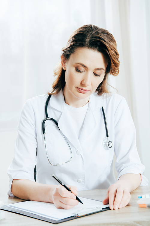 doctor in white coat writing on clipboard in clinic