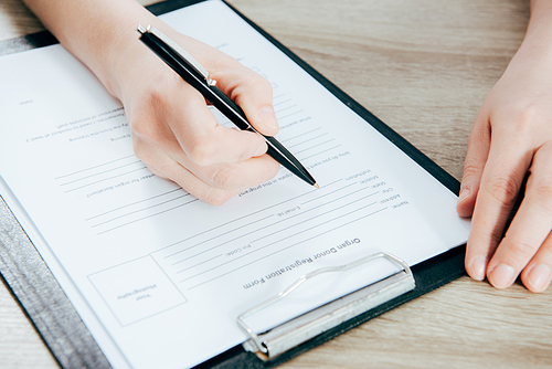 cropped view of donor signing registration form on wooden surface