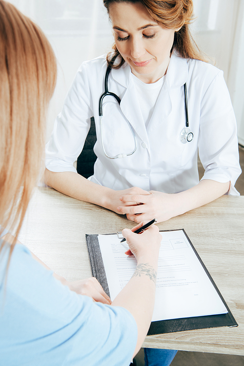 cropped view of donor signing registration form and doctor in white coat