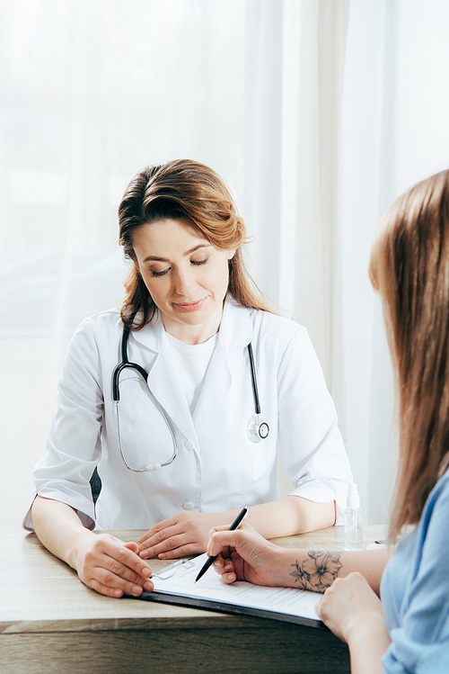 cropped view of donor signing registration form and doctor in white coat