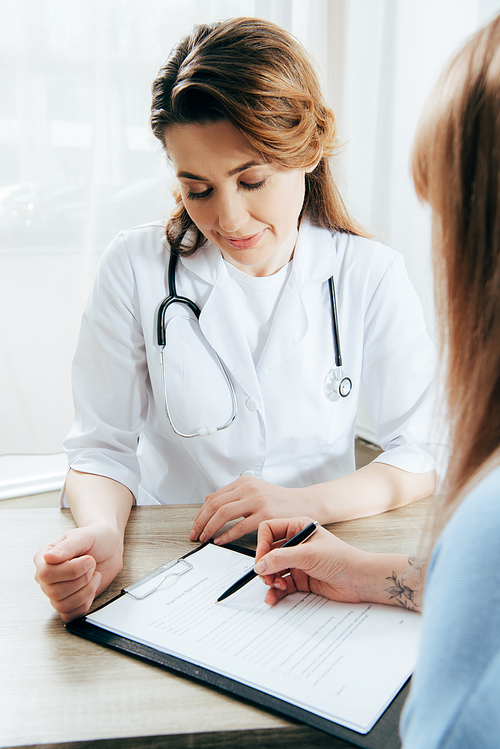 cropped view of donor signing registration form and doctor in white coat