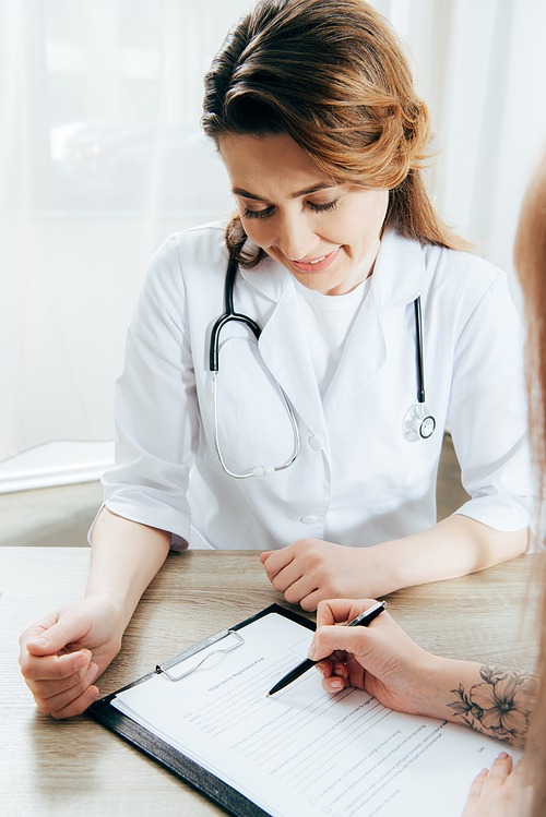 cropped view of donor signing registration form and doctor in white coat