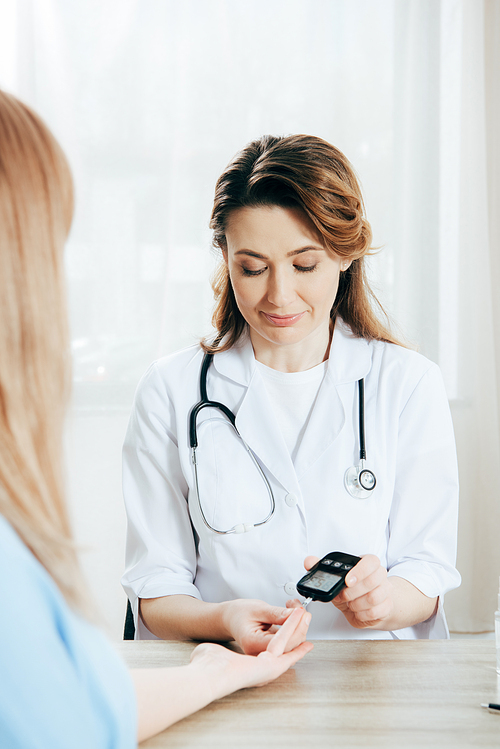 cropped view of donor and doctor measuring glucose level with glucometer