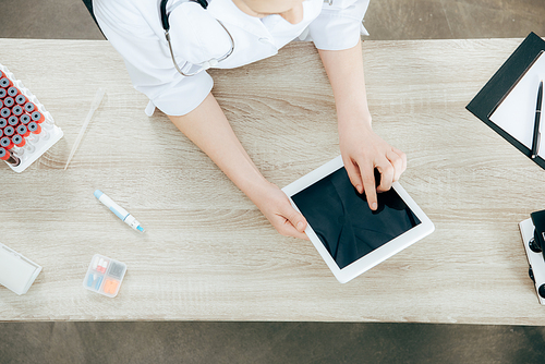 overhead view of doctor in white coat using digital tablet with blank screen