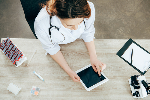 overhead view of doctor in white coat using digital tablet with blank screen