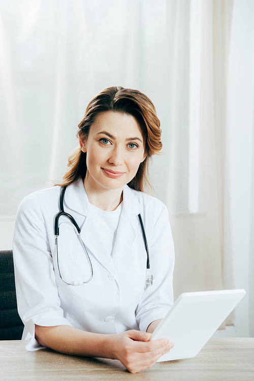 smiling doctor in white coat with stethoscope using digital tablet in clinic