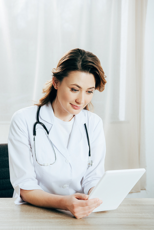 smiling doctor in white coat with stethoscope using digital tablet in clinic