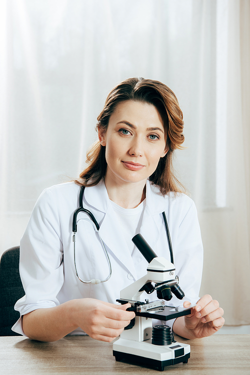 doctor in white coat with stethoscope using microscope in clinic