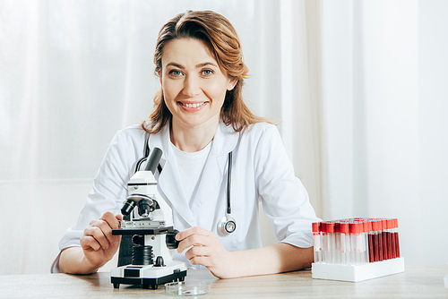 doctor in white coat with stethoscope using microscope in clinic