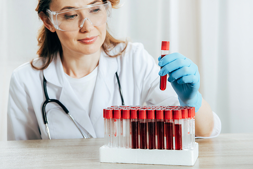 concentrated doctor in protective goggles holding test tube with blood