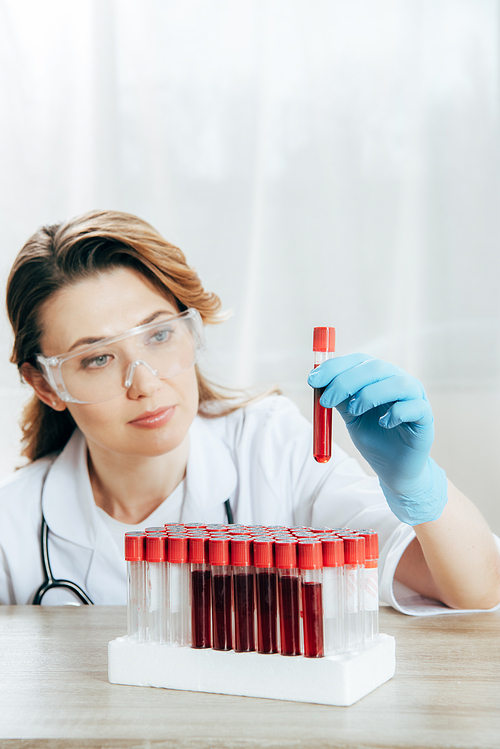 concentrated doctor in protective goggles holding test tube with blood