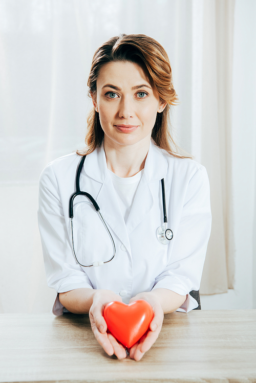 smiling doctor in white coat with stethoscope holding plastic heart