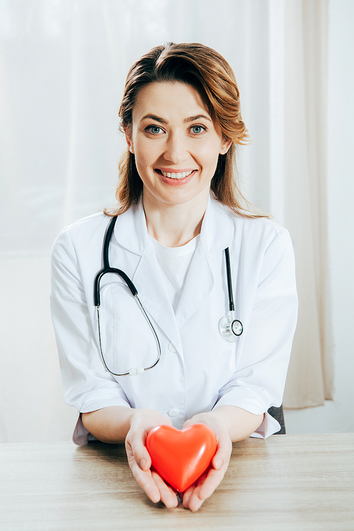 smiling doctor in white coat with stethoscope holding plastic heart