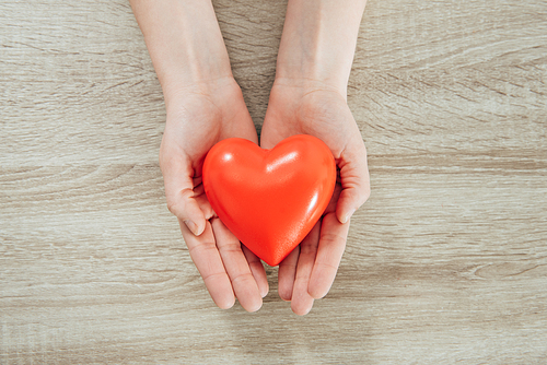 partial view of woman holding plastic heart on wooden surface