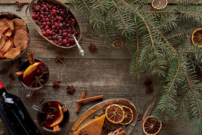 top view of red spiced mulled wine near fir branch, berries, anise, orange slices and cinnamon on wooden rustic table