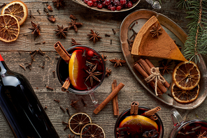 top view of red spiced mulled wine near fir branch, pie, berries, anise, orange slices and cinnamon on wooden rustic table