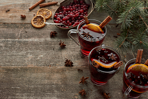 red spiced mulled wine near fir branch, berries, anise, orange slices and cinnamon on wooden rustic table