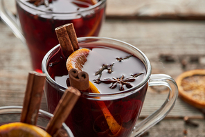 close up view of red spiced mulled wine with berries, anise, orange slice and cinnamon on wooden rustic table