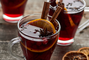 close up view of red spiced mulled wine with berries, anise, orange slice and cinnamon on wooden rustic table